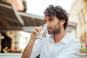 Man in an open-necked shirt with curly textured hair drinking a glass of water